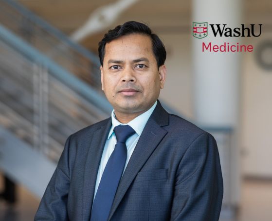A man in a suit and tie stands confidently indoors, in front of a blurred staircase. The WashU Medicine logo is visible in the upper right corner.