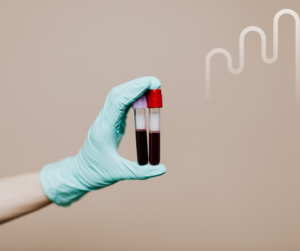 A gloved hand holds two blood-filled test tubes against a beige background, with a subtle white graph design, conveying a clinical, professional tone.